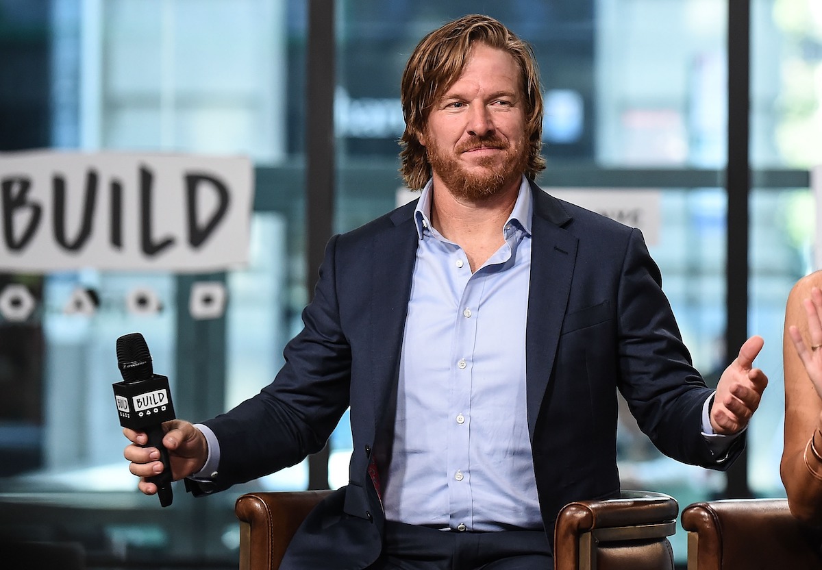 Chip Gaines smiles, holding a microphone during a speaking event.