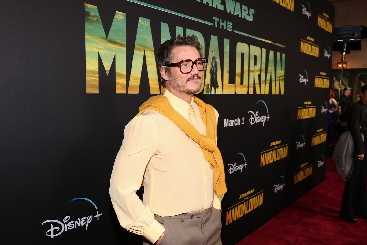 Pedro Pascal poses in front of a backdrop with the logo from "The Mandalorian" season 3.