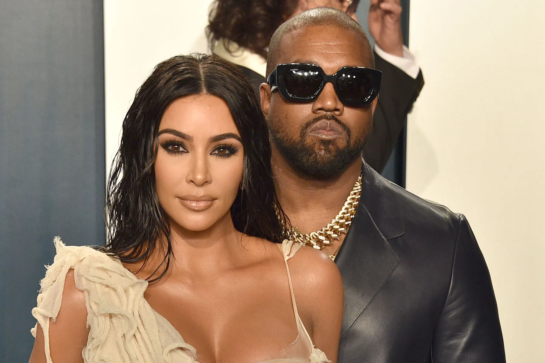 Kim Kardashian in a dress with Kanye West in sunglasses standing behind her at a party in 2020