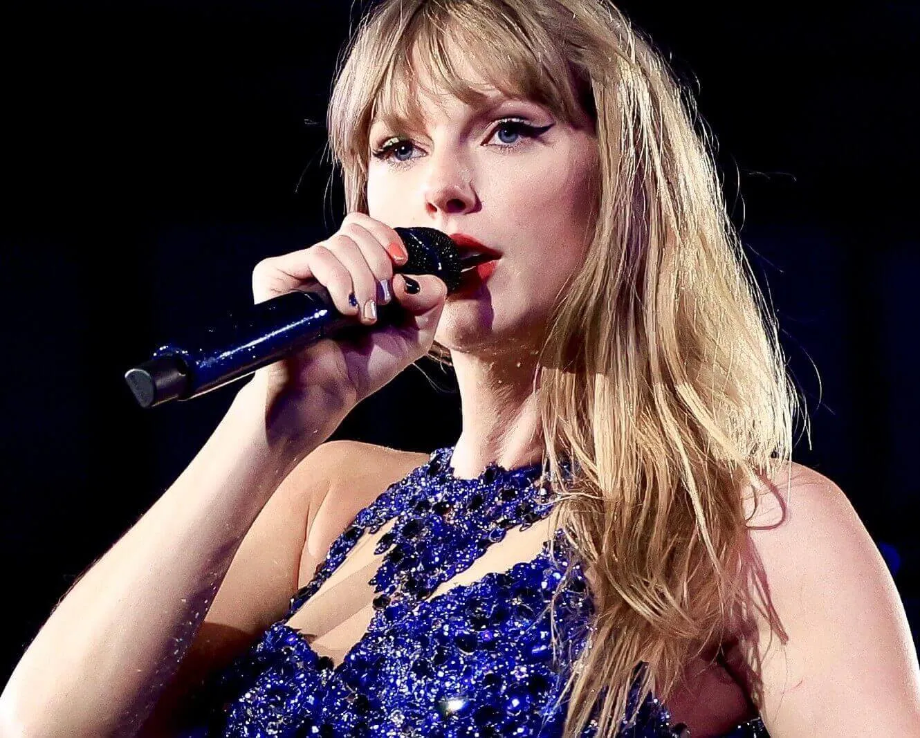 Taylor Swift wears blue sequins and sings into a microphone.